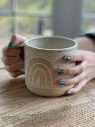 Hands holding a ceramic mug with rainbow decor